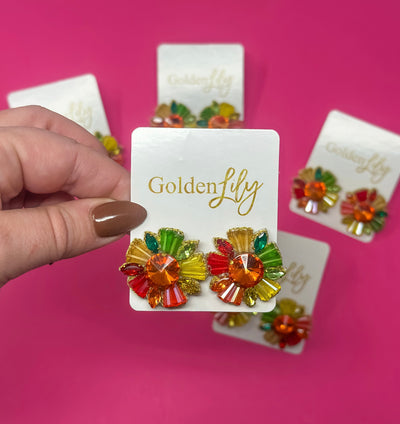 Fall rhinestone burst earrings with orange, red, yellow, and green gems on Golden Lily card against pink background.